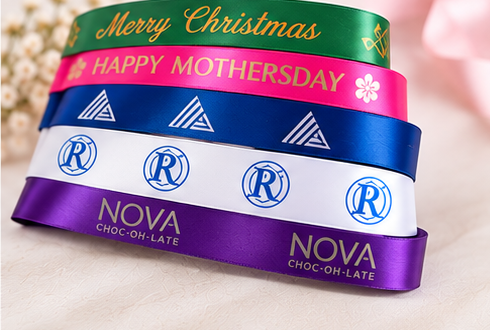 Stacked personalised satin gifting ribbons in green, pink, blue, white and purple with foil messages and logos